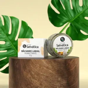 Bálsamo labial humectante Fusión Selvática en tarro de vidrio de 30 gramos y caja, sobre pedestal de madera y fondo decorado con hojas verdes.